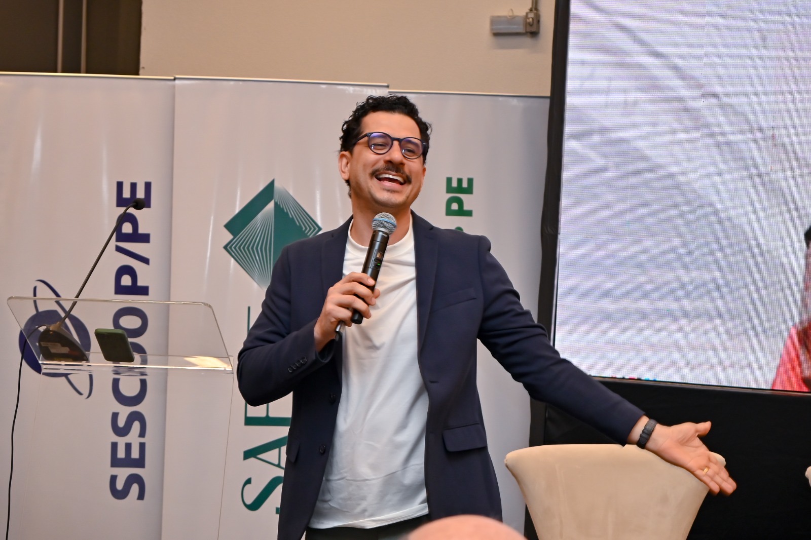 Cleber Zequetto sorrindo e falando ao público durante o Coopanest Day