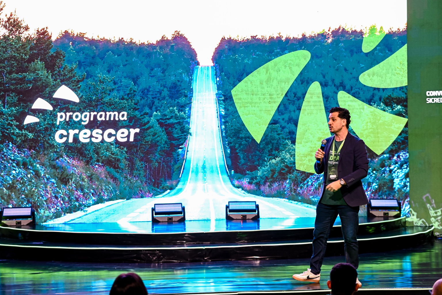 Cleber Zequetto com microfone, palestrando em um palco